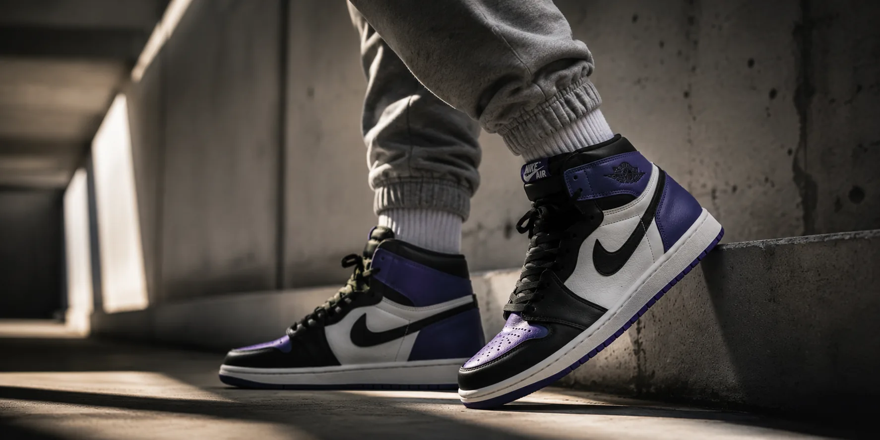 Air Jordan 1 Court Purple sneakers worn on-foot against concrete architecture